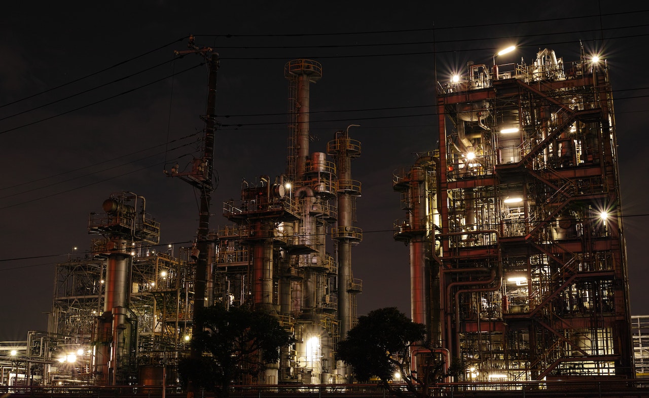  An oil refinery plant with many pipes and structures lit up at night, representing the search query 'Quality Control Fresh Graduate'.